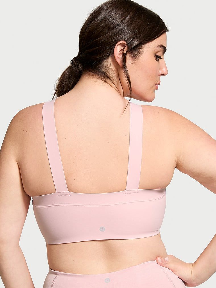 Modelka prezentuje biustonosz sportowy VS Elevate Cross-Strap Bandeau. Produkt ma kolor różowy i pochodzi z kolekcji VSX.