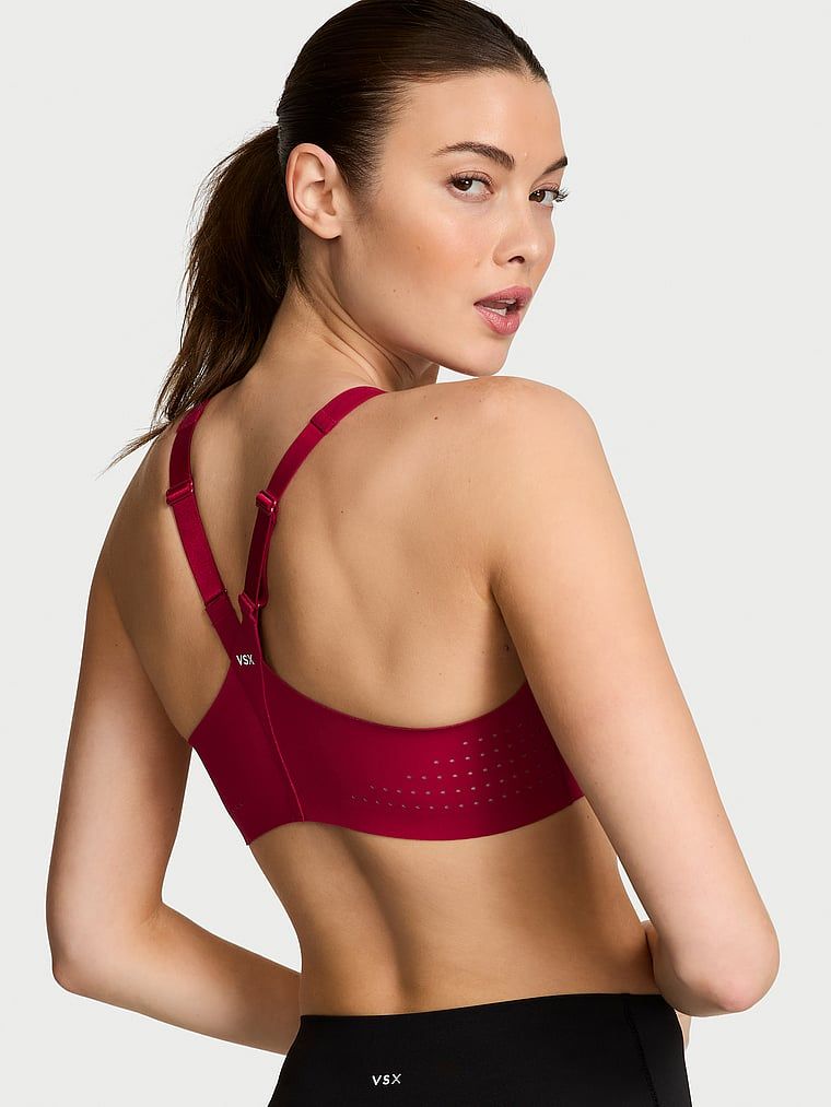 Modelka prezentuje biustonosz sportowy z maksymalnym podtrzymaniem z suwakiem Featherweight Max Front-Close. Produkt ma kolor czerwony i pochodzi z kolekcji VSX.