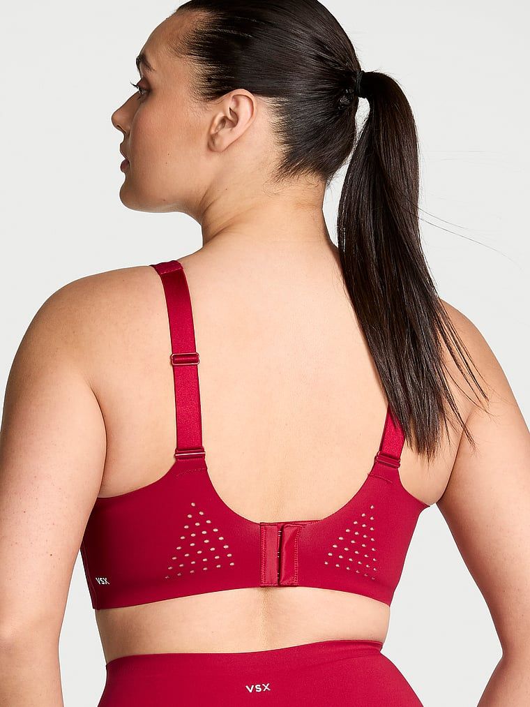 Modelka prezentuje biustonosz sportowy z maksymalnym podtrzymaniem Featherweight Max. Produkt ma kolor czerwony i pochodzi z kolekcji VSX.