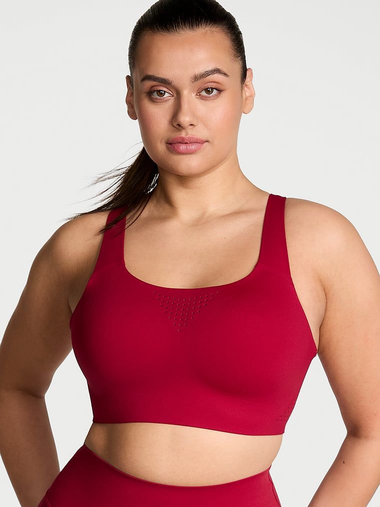 Modelka prezentuje biustonosz sportowy z maksymalnym podtrzymaniem Featherweight Max. Produkt ma kolor czerwony i pochodzi z kolekcji VSX.