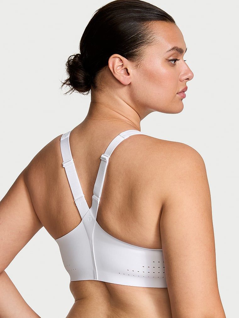 Modelka prezentuje biustonosz sportowy z maksymalnym podtrzymaniem z suwakiem Featherweight Max Front-Close. Produkt ma kolor biały i pochodzi z kolekcji VSX.