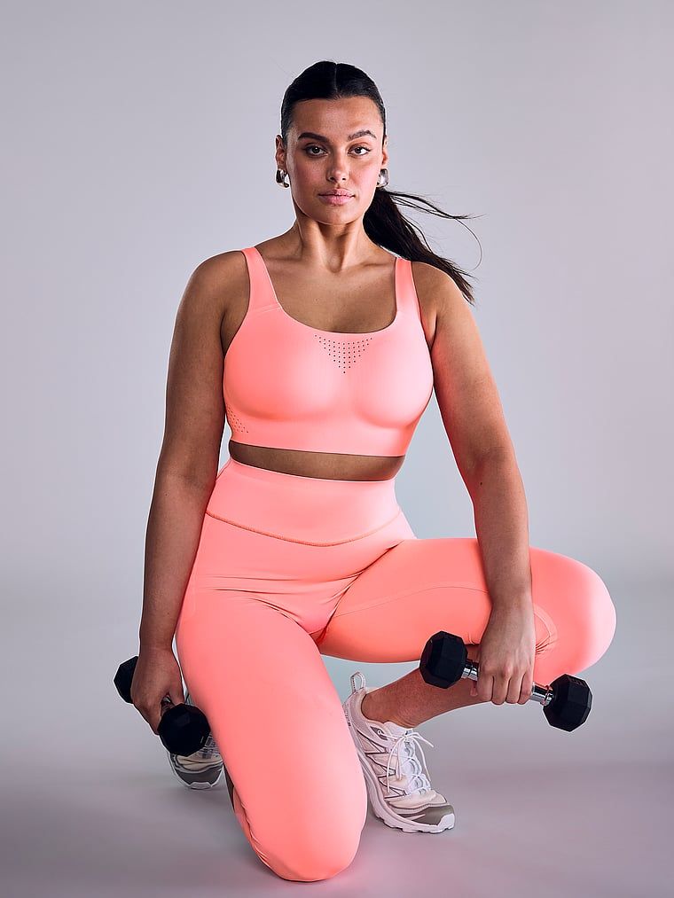 Modelka prezentuje biustonosz sportowy z maksymalnym podtrzymaniem Featherweight Max. Produkt ma kolor czerwony i pochodzi z kolekcji VSX.